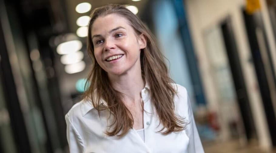 A smiling woman in a white shirt in a bright office corridor